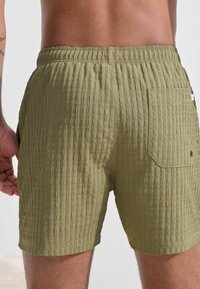 Olivengrüne strukturierte Badeshorts mit elastischem Bund, Gesäßtasche und einem dezenten gerippten Muster für zusätzliche Details.