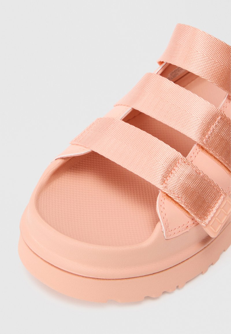 Pfirsichfarbene Sandalen mit drei breiten, strukturierten Riemen und einer geformten Gummisohle. Glatte Oberfläche mit einem flachen Design und rutschfester Sohle.