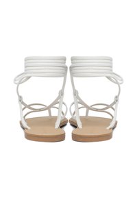 Sandali bianchi con cinturini sottili incrociati e una suola piatta color biscotto. Il design presenta diversi anelli alla caviglia per un supporto extra.