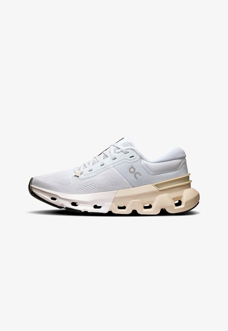 Chaussure de sport blanche avec une tige en mesh respirant, une semelle intermédiaire rembourrée en crème et une semelle extérieure en caoutchouc noir texturé. Détail de logo minimaliste.