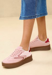 Baskets en suede rose avec un doublure blanche et des accents rouges. Semelle plateforme en marron. Présente un design cousu et des perforations sur le côté.