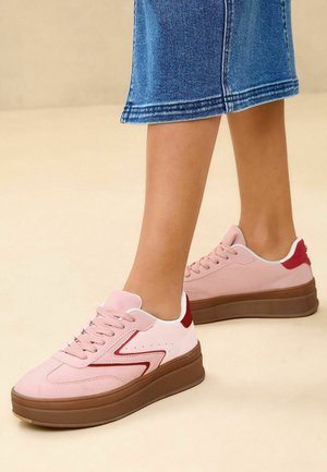 Baskets en suede rose avec un doublure blanche et des accents rouges. Semelle plateforme en marron. Présente un design cousu et des perforations sur le côté.