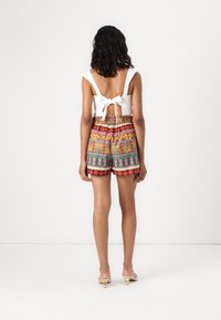 Biała, bezrękawnikowa bluzka z kokardą z tyłu, w zestawieniu z kolorowymi, wzorzystymi szortami z kwiatowymi motywami i elastycznym paskiem.