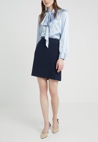 Light blue satin blouse with a tied neckline, long sleeves; navy textured skort with two black accents; beige heels with a bow detail.
