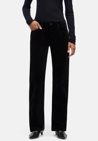 Czarne spodnie sztruksowe o prostym kroju nogawki, z przednimi kieszeniami i teksturowanym wykończeniem. Noszone z dopasowanym ciemnym topem i butami na obcasie.