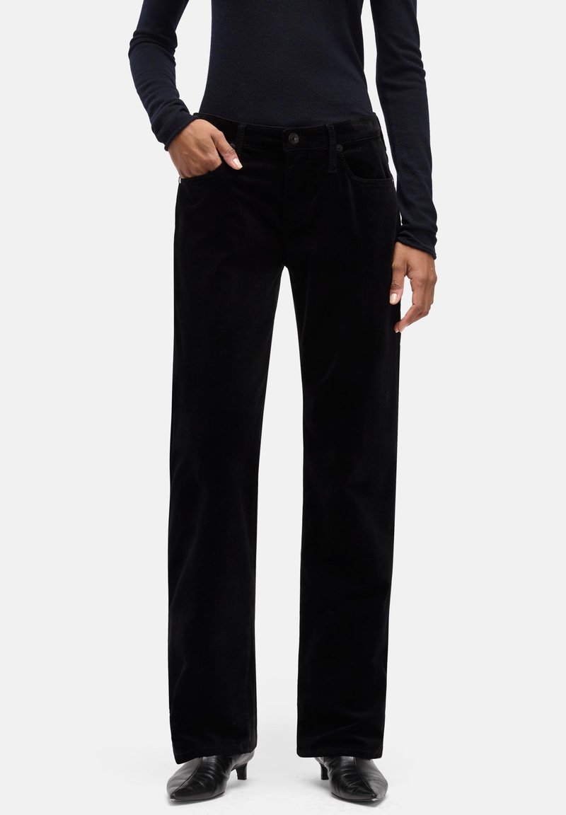 Czarne spodnie sztruksowe o prostym kroju nogawki, z przednimi kieszeniami i teksturowanym wykończeniem. Noszone z dopasowanym ciemnym topem i butami na obcasie.