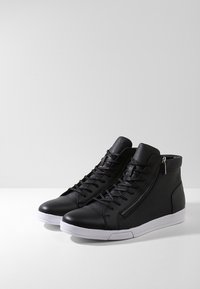 Černé vysoké tenisky z kůže s předním šněrováním, bočním zipem a bílou gumovou podrážkou. Hladká textura s minimálními detaily.