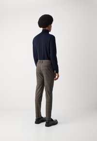 Námornícky dlhý rukáv s vysokým golierom, spárovaný s hnedými nohavicami s kostkovaným vzorom a čiernymi slip-on topánkami, z pohľadu zozadu.