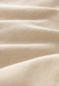 Beige stof med en struktureret overflade, der har skrå ribber og bløde folder, hvilket skaber et glat og ensartet udseende.