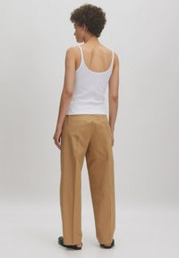 Witte mouwloze top gecombineerd met hooggerokte, losse beige broek en zwarte platte sandalen. De stof lijkt glad met minimale details.