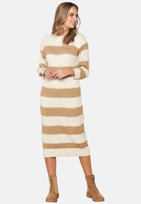 Abito lungo a maglia con strisce orizzontali beige e marrone chiaro. Presenta un collo a giro e maniche lunghe, abbinato a stivali alla caviglia color tan.
