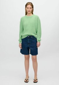 Mintgrüner Strickpullover mit gerippter Textur, kombiniert mit dunklen Jeansshorts. Das Outfit wird mit Flip-Flop-Sandalen abgerundet.