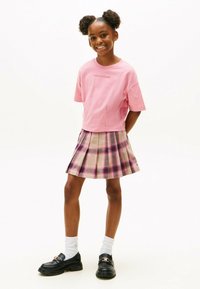 Rosa bomulds t-shirt med korte ærmer, parret med en beige og ternet plisseret nederdel med lilla accenter. Sorte loafers og hvide sokker.