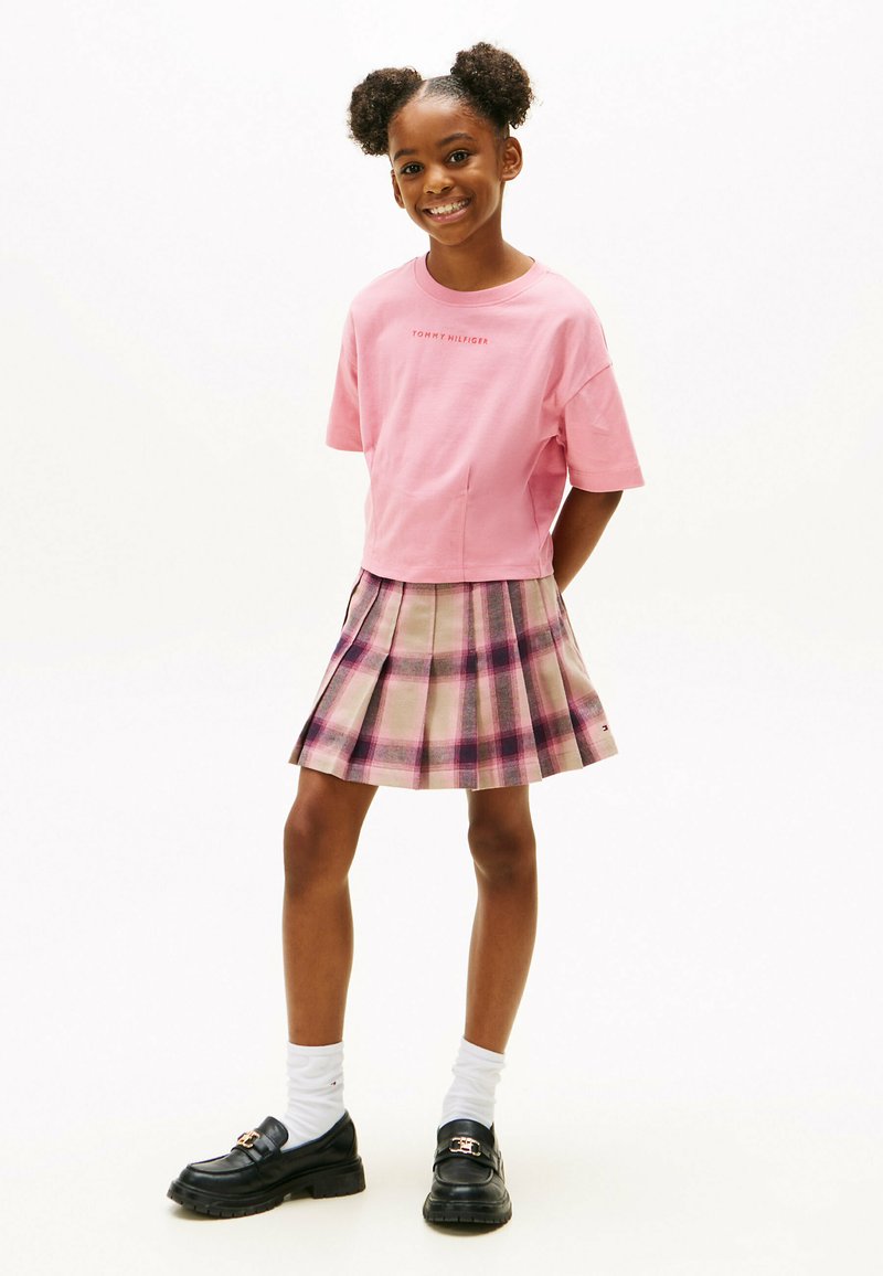 Rosa bomulds t-shirt med korte ærmer, parret med en beige og ternet plisseret nederdel med lilla accenter. Sorte loafers og hvide sokker.