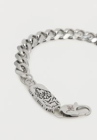 Ασημένιο βραχιόλι αλυσίδα με χαραγμένο πρόσωπο τίγρη σε ορθογώνια πλάκα και κούμπωμα σπαστού γαρίδα με χαραγμένα αρχικά σε λευκό φόντο.