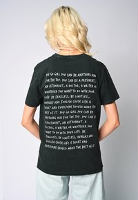 Crna pamučna majica s velikim bijelim natpisima na leđima koji sadrže inspirativne fraze. Kratki rukavi i klasičan kroj s okruglim vratom.