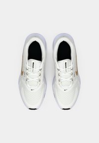 Scarpe da corsa Nike bianche con tomaia texturizzata, lacci piatti e logo swoosh dorato sul lato. Suola leggera con interno nero.