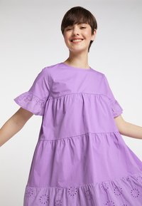 Lilla bomulds kjole med korte, flagrende ærmer, lagdelt design og broderede detaljer i kanten. Glat tekstur og afslappet pasform.