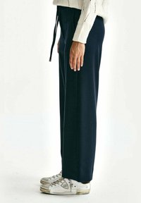Marineblauwe wijde broek met een trekkoord in de taille, gecombineerd met witte sneakers. Soepele stof, rechte pasvorm en minimale details.
