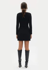 Czarna dzianinowa sukienka z długimi rękawami, prążkowaną teksturą, dopasowanym krojem i długością powyżej kolan, zestawiona z wysokimi czarnymi botkami na obcasie.