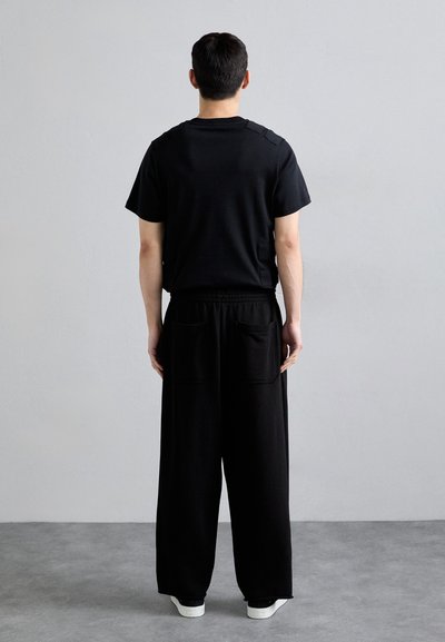 Schwarzes Baumwoll-T-Shirt mit kurzen Ärmeln und gesteppten Schulterdetails, kombiniert mit lockeren schwarzen Hosen mit großen Gesäßtaschen.