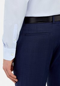 Lichtblauw en wit gestreepte overhemden met knoopjes aan de mouwen, gecombineerd met donkerblauwe, gestructureerde broek met een achterzak en een zwarte riem.