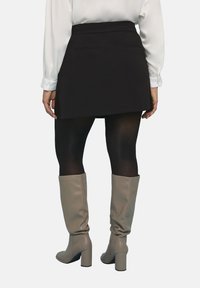 Minifalda negra con una cintura ajustada y dos bolsillos traseros, combinada con botas beige hasta la rodilla y medias negras. Textura suave en toda la prenda.