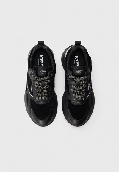 Schwarze Sneakers aus einer Kombination von glattem Leder und weichem Wildleder, mit strukturierten Schnürsenkeln und einer gepolsterten Sohle. Logo auf der Zunge sichtbar.