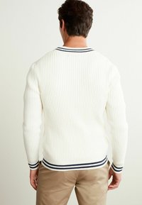 Pull blanc côte avec un col et des poignets rayés bleu marine et blanc, doté de manches longues et d'une silhouette ajustée.