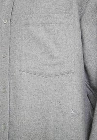 Grå skjorta med knappar, tillverkad av strukturerad ull, med en bröstficka och subtil logobrodyr nära fållen.