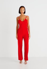 Rød, ermeløs jumpsuit med dyp utringning og vide ben. Glatt stoff, tettsittende midje og minimale sømdetaljer.