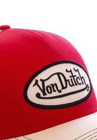 Gorra roja con una corona redondeada, con un prominente parche ovalado cosido en negro que dice "Von Dutch". La visera tiene un lado inferior beige.