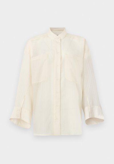 Ελαφρύ κρεμ πουκάμισο με κουμπιά, με γιακά μανταρίνι, δύο μπροστινές τσέπες και διακριτικές κάθετες ρίγες. Μαλακό ύφασμα, άνετη εφαρμογή, μανίκια μισού μήκους.