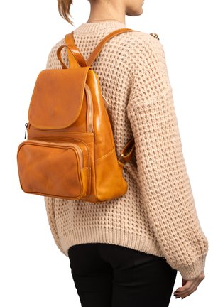 Zaino in pelle marrone chiaro con chiusura a patta, tasca anteriore con zip e spallacci regolabili. Texture morbida e forma strutturata, indossato sulla schiena.
