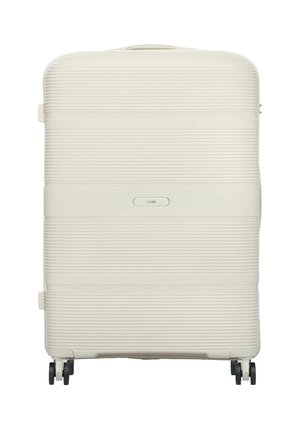 Duża walizka o twardej skorupie w kremowym kolorze z poziomymi żłobieniami, cztery czarne obrotowe kółka i górny uchwyt.