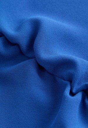 Tessuto blu texture con morbidi drappeggi fluenti e una superficie liscia, evidenziando un colore intenso e una lucentezza sottile.