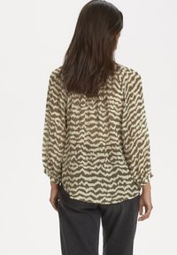Blouse légère et transparente avec un motif abstrait en zigzag olive et crème, dotée de manches longues et d'un détail froncé au dos.