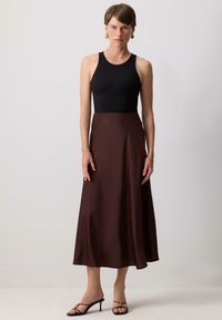 Débardeur noir côtelé associé à une jupe midi fluide en satin marron, présentant une texture lisse et une silhouette subtile en A.