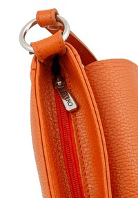 Orange leather bag with textured finish, featuring a silver ring, red zipper, and a metal logo tag. Close-up view of opening detail.
