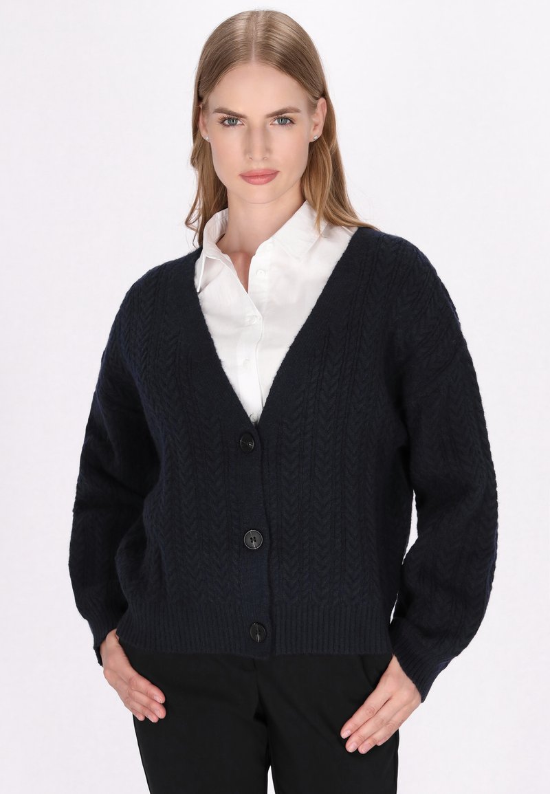 Navyblauwe gebreide cardigan met een V-hals, oversized mouwen en vijf grote zwarte knopen. Heeft een gestructureerd patroon en een geribde zoom.