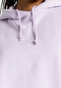 Ljuslila Nike-hoodie med dragsko och en liten vit logotyp på bröstet, tillverkad av mjukt, texturerat tyg.