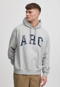 Hoodie gris en matériau doux, arborant un grand imprimé "ARC" usé en marine et un graphique circulaire près de la taille.