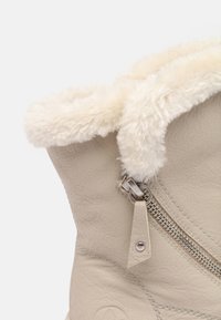 Primo piano di un stivaletto in pelle beige per l'inverno, con rivestimento in pelliccia sintetica di colore crema e una zip laterale con una linguetta in pelle.