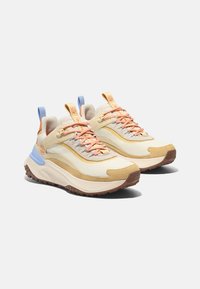 Beige och cremefärgade sportskor med en texturerad ovandel i tyg, orange och blå accenter samt en tjock, räfflad gummisula.