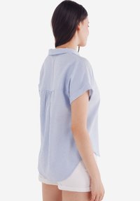 Blusa a righe blu chiaro con maniche corte, una piega sul retro e un orlo curvo. Realizzata in tessuto morbido, presenta un colletto classico.