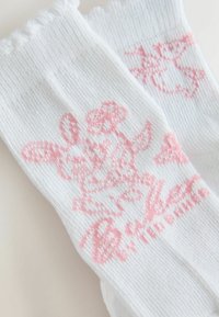 Chaussettes blanches avec un personnage de dessin animé rose et des motifs floraux, mettant en scène un lapin ludique et un texte en écriture cursive sur un tissu côtelé.