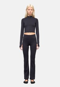 Zwarte cropped zip-up lange mouw top gecombineerd met zwarte high-waisted strak zittende broek. Gladde textuur met rekbare stof; geen zichtbare logo's.