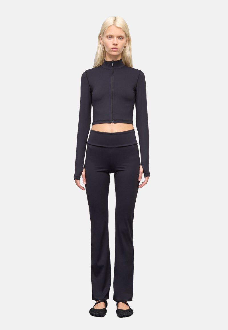 Zwarte cropped zip-up lange mouw top gecombineerd met zwarte high-waisted strak zittende broek. Gladde textuur met rekbare stof; geen zichtbare logo's.