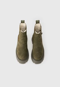 Un paio di stivali alla caviglia in suede verde oliva con suole di gomma spessa e rivestimento in fleece color crema, visti dall'alto su sfondo bianco.
