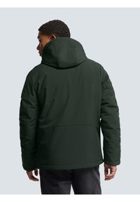 Dark green puffer jacket with a large hood, featuring visible seams and a smooth exterior texture. Simple design; no visible logos.